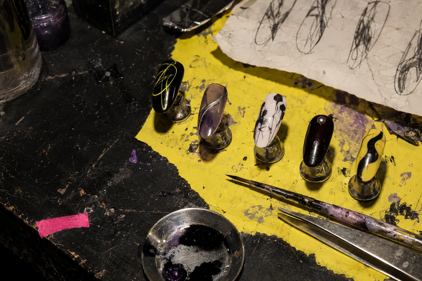 Concept artwork of five nail designs on an artist's paint-marked workbench, with sketches and tools
